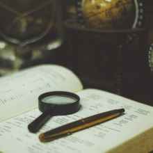 A book, magnifying glass and pen with a globe in the background - tools for language learning