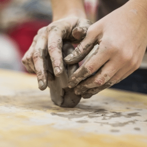 A person moulding a lump of clay with their hands, making art